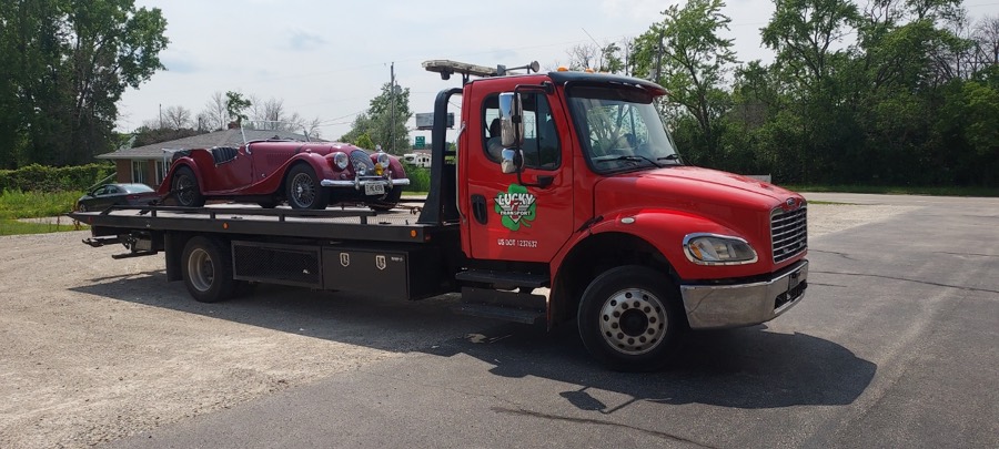 Red Lucky 7 flatbed truck carrying a classic Morgan roadster